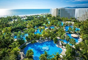 Ett semesterparadis med flera pooler, omgivet av palmer, en strand och en stor hotellbyggnad.