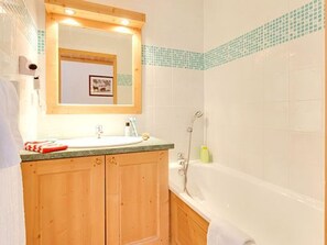 A bathroom with a wooden vanity, a sink, a mirror, and a bathtub. - Spacious apartment, ski-in/ski-out - 6 guests (Les Menuires)