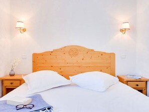 A neatly made bed with white linens, two bedside lamps, a wooden headboard, and a small bedside table with a vase of flowers. - Spacious apartment, ski-in/ski-out - 6 guests (Les Menuires)
