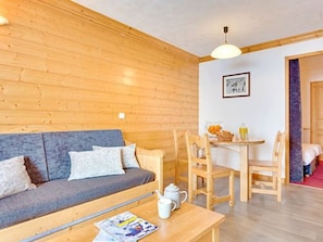 A cozy room with a wooden wall, a sofa, a table with a magazine, and a breakfast setup. - Ideal apartment, ski-in/ski-out - 4 guests (Les Menuires)