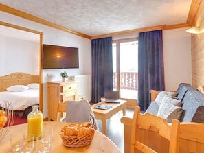 A room with a bed, a sofa, a dining table with breakfast items, and a TV mounted on the wall. - Ideal apartment, ski-in/ski-out - 4 guests (Les Menuires)