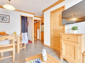 A room with wooden flooring, a dining table with chairs, a television mounted on the wall, and a small cabinet. - Ski-in ski-out chalet - 4 guests (Les Menuires)