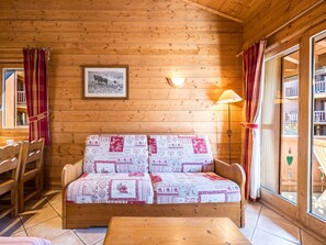 A wooden cabin interior with a sofa, a table, and a framed picture on the wall. - Spacious apartment - 6 guests (Les Menuires)