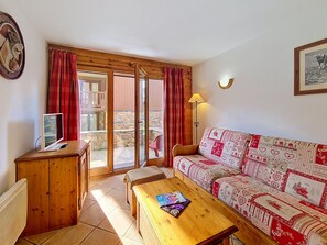Een gezellige woonkamer met een houten bureau, een bank met een gestreept hoesje, en een schuifdeur naar een buitenruimte.