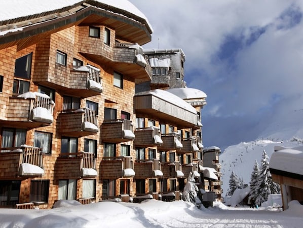 Un hotel de varios pisos con balcones y una pista de esquí al fondo.