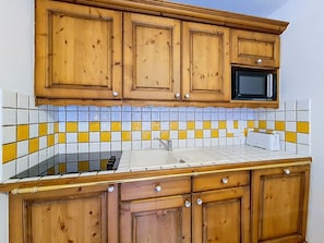 Eine Küche mit Holzschränken, einer Mikrowelle, einem Spülbecken und einer gefliesten Spritzschutzwand.