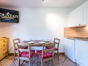 A dining area with a wooden table, four chairs with red cushions, and a white cabinet. - Renovated studio cabin, mountain view (Les Menuires)