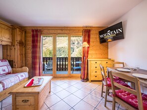 Une pièce chaleureuse avec un décor intérieur en bois, une table à manger avec des chaises, un canapé et un téléviseur fixé au mur.