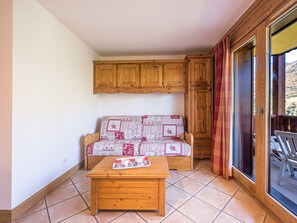 Une pièce chaleureuse avec un canapé en bois, une petite table en bois et une porte-fenêtre coulissante donnant sur un espace extérieur.