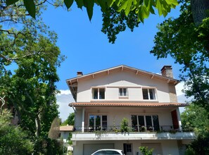A two-story house with a balcony, surrounded by trees.