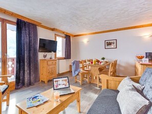 A cozy living room with a sofa, a coffee table with a laptop, a dining area with chairs, and a kitchen area with a counter. - Spacious apartment, southwest - 8 guests (Les Menuires)