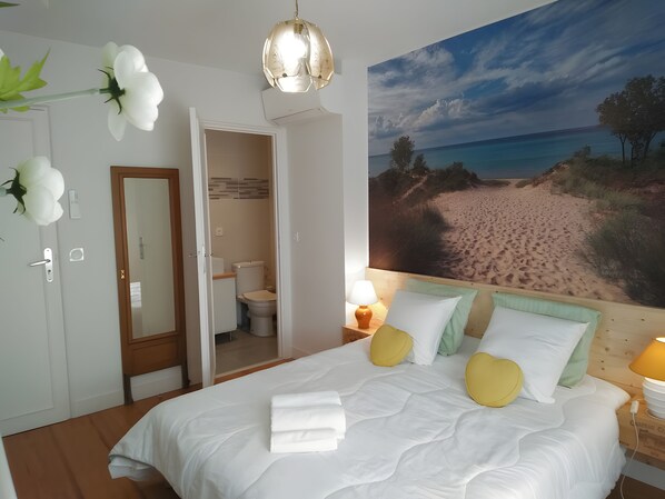 A hotel room with a bed, a bathroom, and a beach mural on the wall.