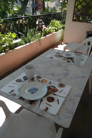 Ein Essbereich im Freien mit einem Tisch für zwei Personen, ausgestattet mit einer weißen Tischdecke, Tellern, Besteck und einer Tasse.