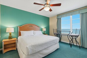 A hotel room with a bed, two bedside tables with lamps, a ceiling fan, a window with curtains, and a view of the ocean. - ☀️Ocean Front Condo with Expansive Views-Daytona Ocean Walk Resort 2023 A/B☀️ (Daytona Beach)