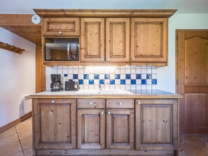 A kitchen with wooden cabinets, a tiled backsplash, and a coffee maker. - Cozy apartment in Les Menuires - 4 guests (Les Menuires)