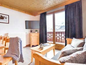 Een knus vertrek met een houten plafond, een televisie, een houten kast, een bank en een raam met gordijnen.