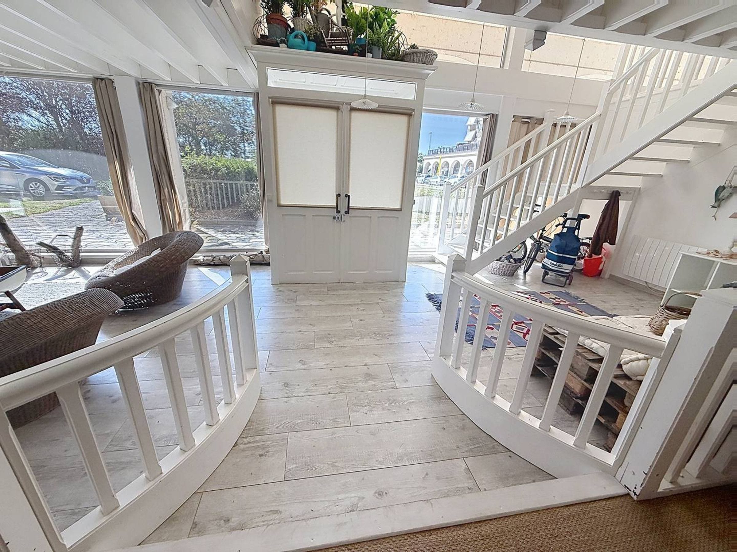 Un intérieur spacieux avec un escalier blanc, une vue sur l’extérieur et un coin salon avec un fauteuil.