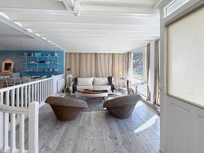Ett takförsett utomhusområde med sittplatser, bestående av en soffa, två fåtöljer i rotting och ett matbord med stolar.
