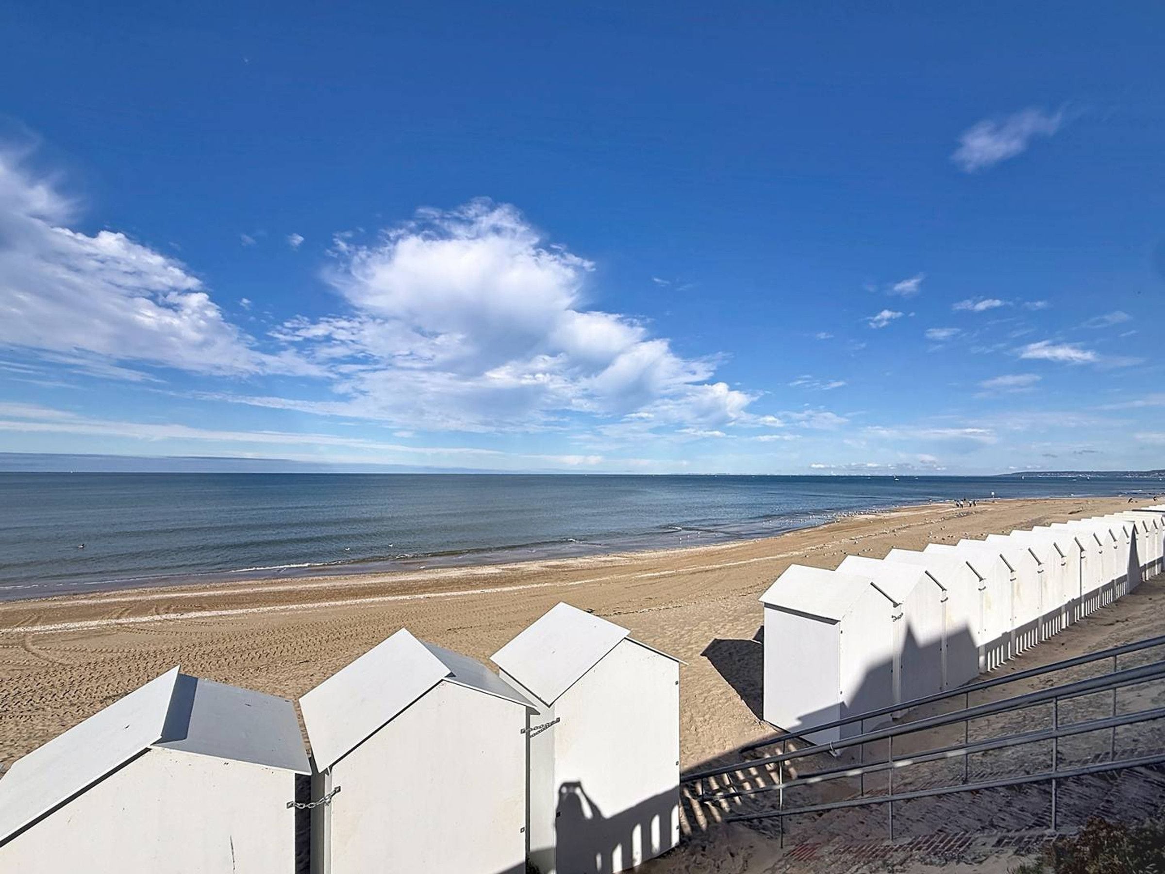 Een strand met een rij witte gebouwen, mogelijk strandhutten, en een heldere lucht.