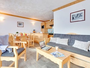 A cozy living room with a sofa, chairs, a coffee table, and a kitchen area in the background. - Spacious ski-in/ski-out apartment - 7 guests (Les Menuires)