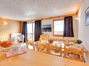 A dining area with wooden furniture, a table set for two, and a television mounted on the wall. - Spacious apartment, ski-in/ski-out - 8 guests (Les Menuires)