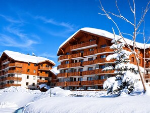 A multi-story wooden building with balconies, surrounded by snow. - Spacious apartment, ski-in/ski-out - 8 guests (Les Menuires)