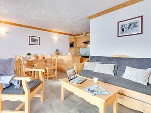A cozy living room with a sofa, chairs, a coffee table, and a kitchen area in the background. - Spacious apartment, ski-in/ski-out - 8 guests (Les Menuires)
