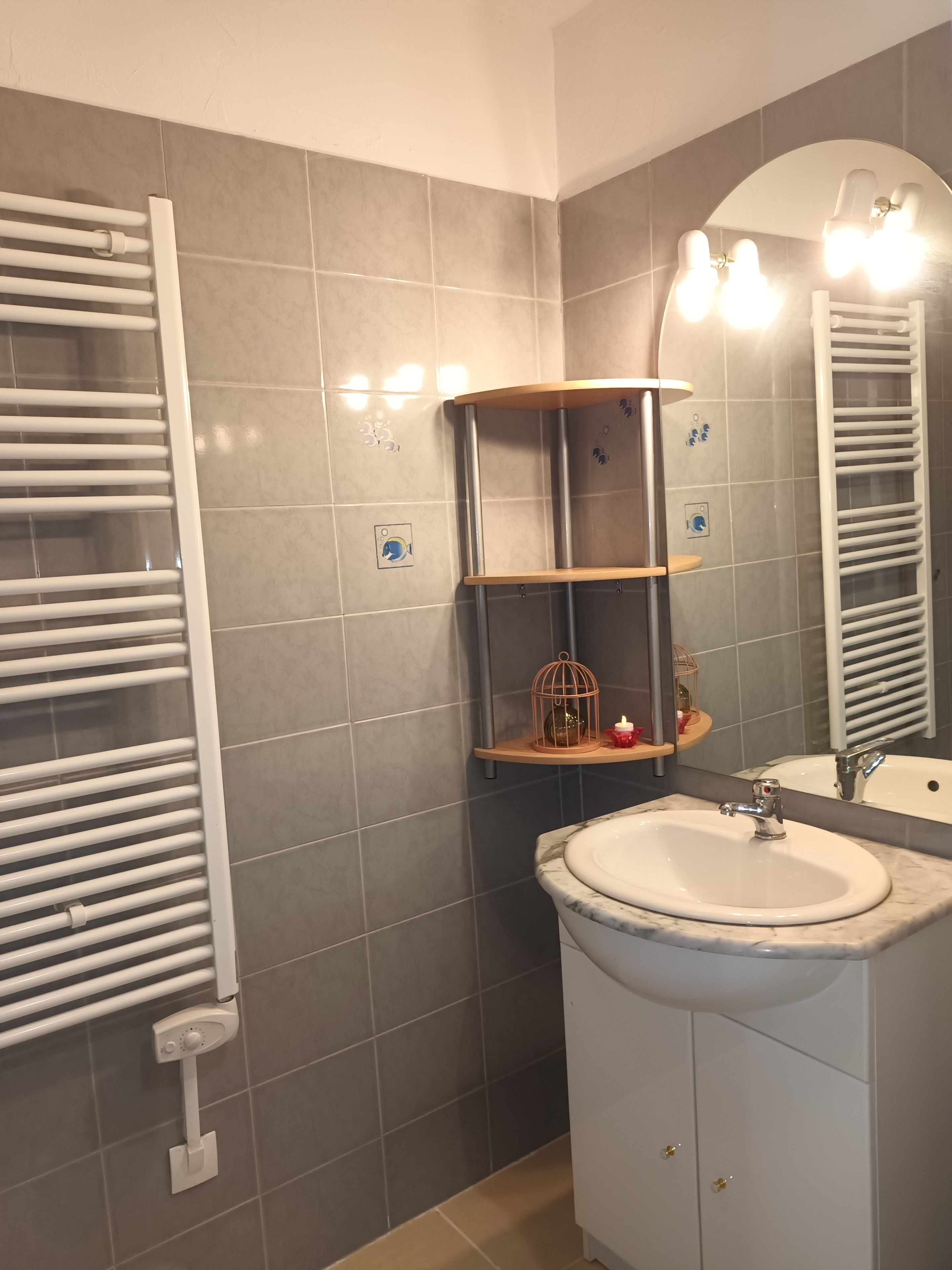 Un baño con un lavamanos blanco, un espejo, un perchero para toallas y una repisa con una jaula de pájaros.