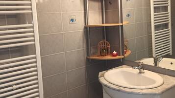 Un baño con un lavamanos blanco, un espejo, un perchero para toallas y una repisa con una jaula de pájaros.