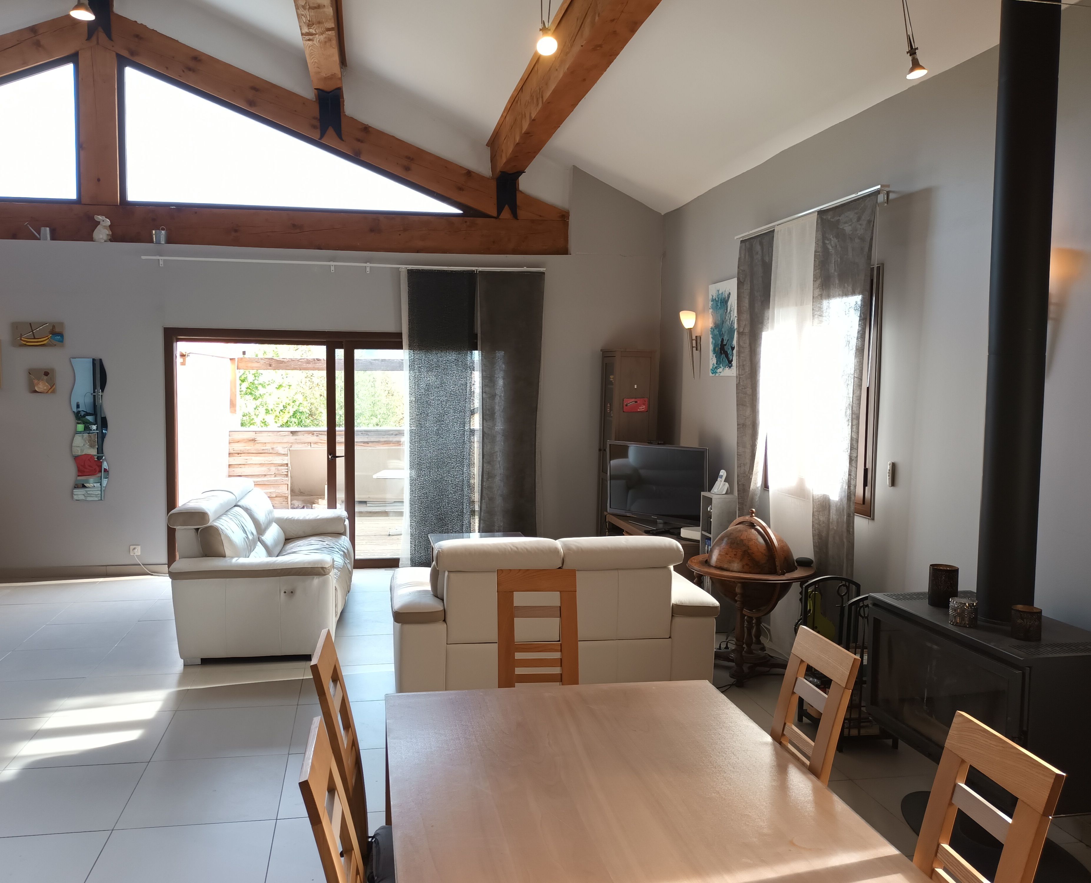 A spacious living room with a high ceiling, wooden beams, a fireplace, a television, and a dining area with a table and chairs.