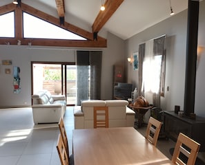 A spacious living room with a high ceiling, wooden beams, a fireplace, a television, and a dining area with a table and chairs.