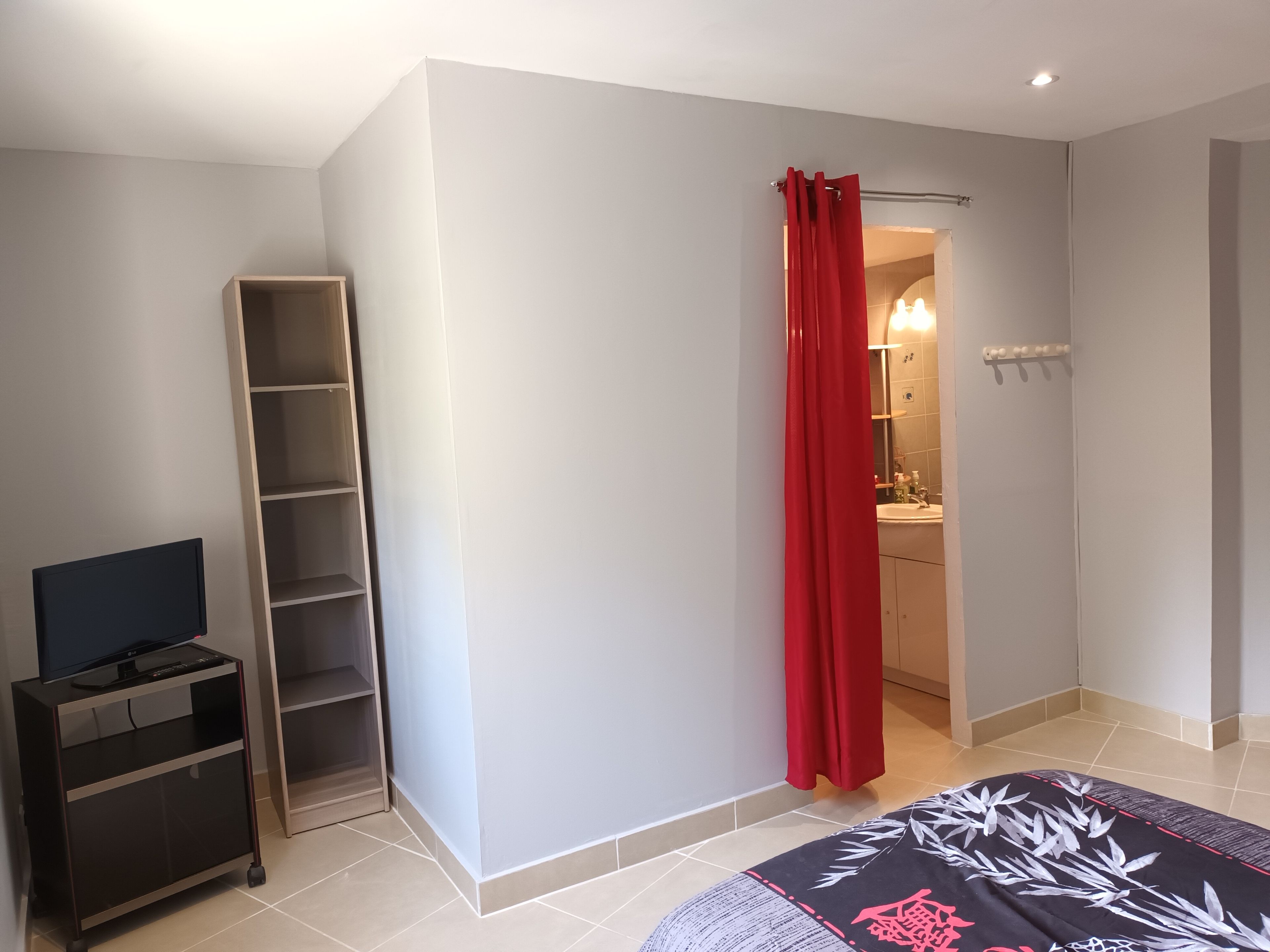 A room with a TV on a stand, a wardrobe, a red curtain, and a bathroom visible through an open door.