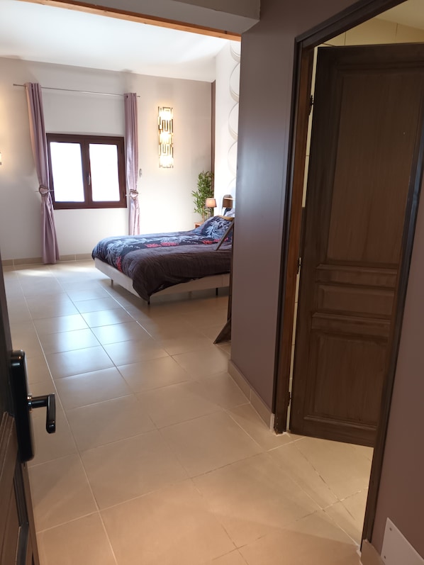 A bedroom with a bed, a window with curtains, a bedside lamp, and a door.