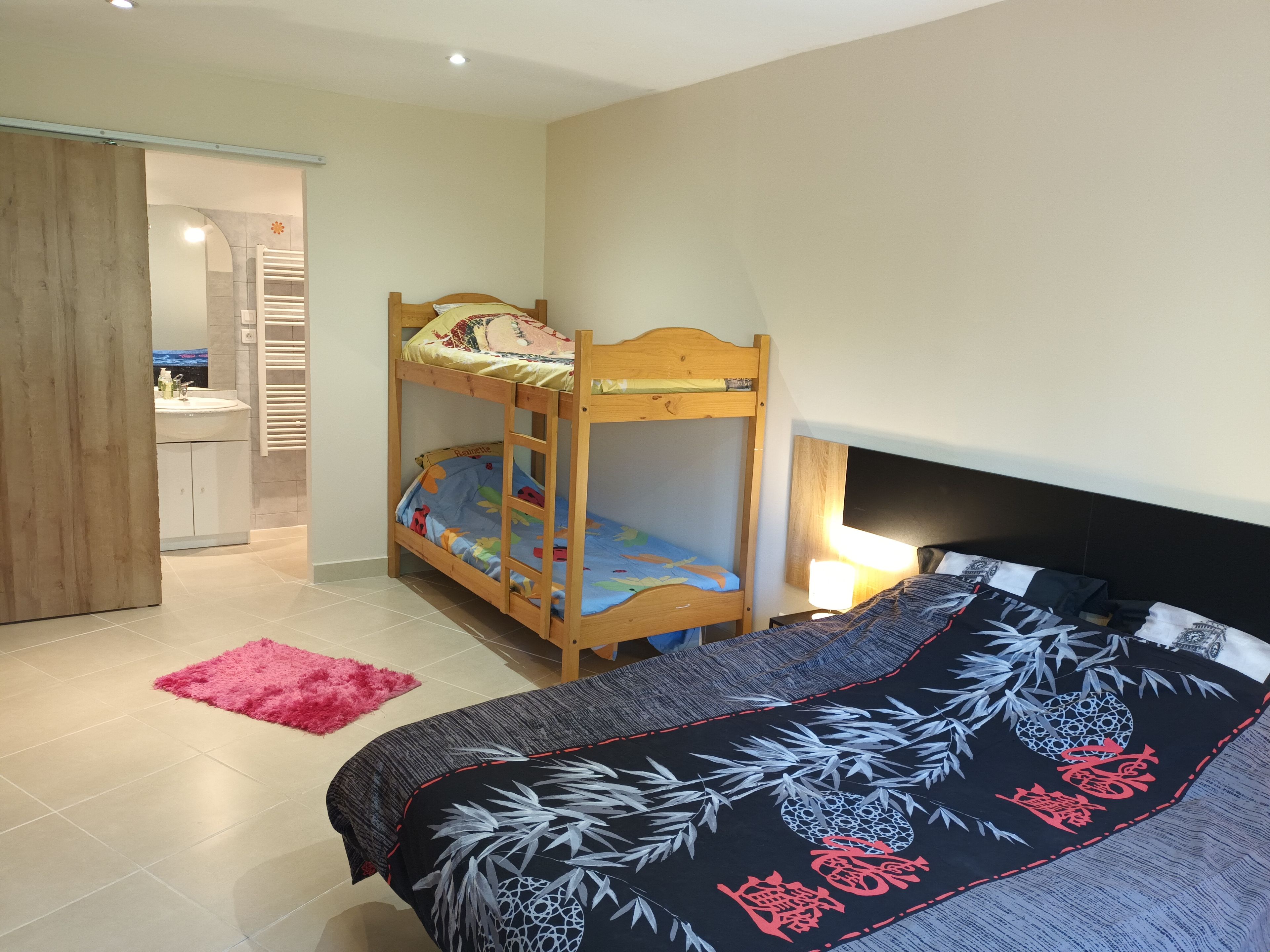 Een slaapkamer met een stapelbed, een nachtkastje met een lamp en een roze vloerkleed.