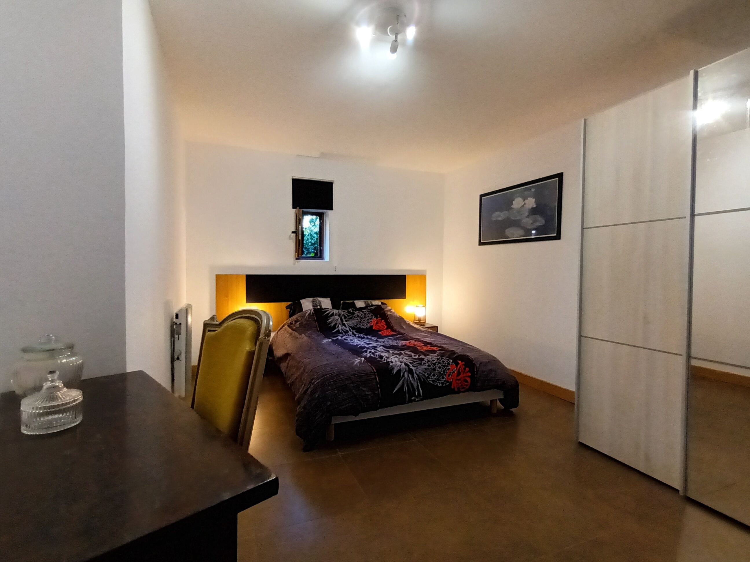 A bedroom with a bed, bedside table, chair, wardrobe, and a window with a view.