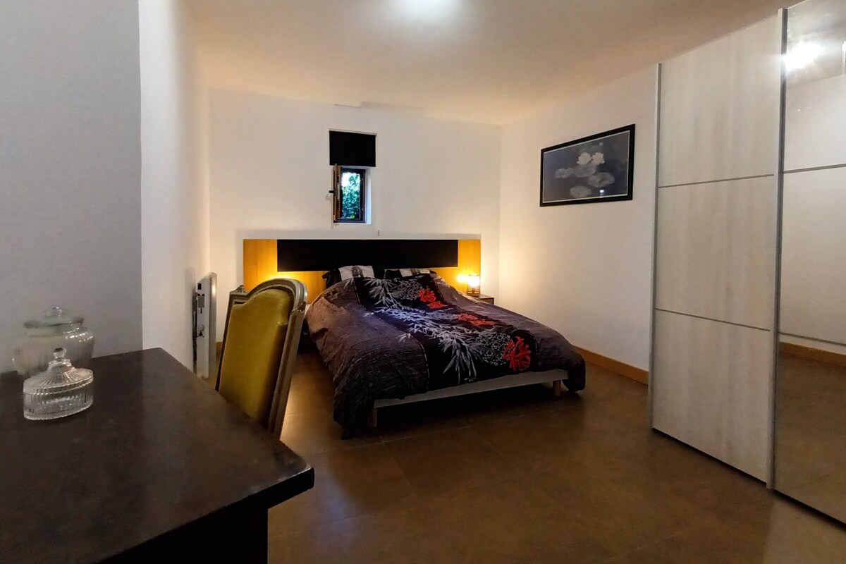 A bedroom with a bed, bedside table, chair, wardrobe, and a window with a view.