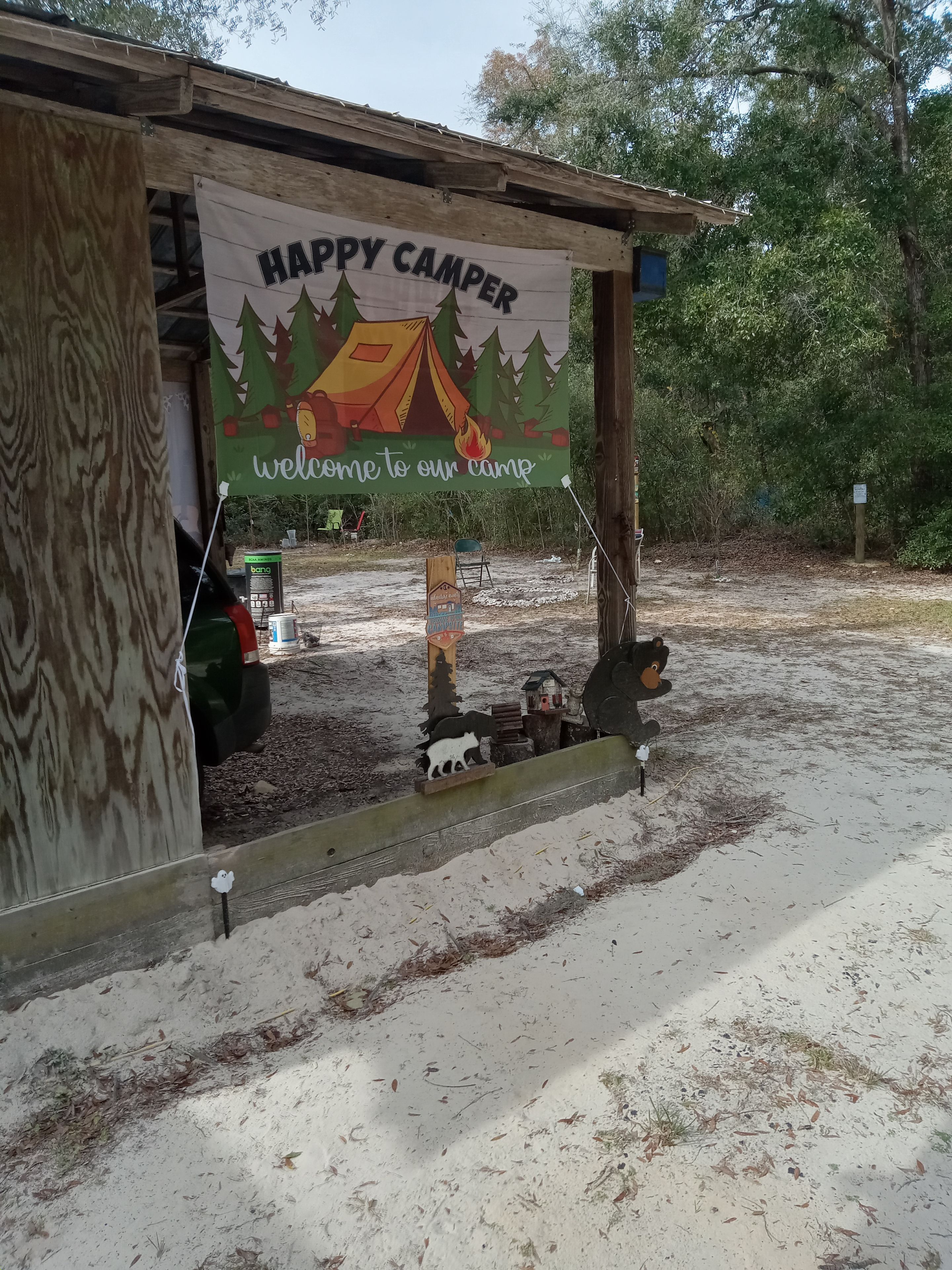 Une structure en bois sur laquelle est accrochée une banderole avec l’inscription : « BIENVENUE, CHERS CAMPEURS, à notre campement ! »