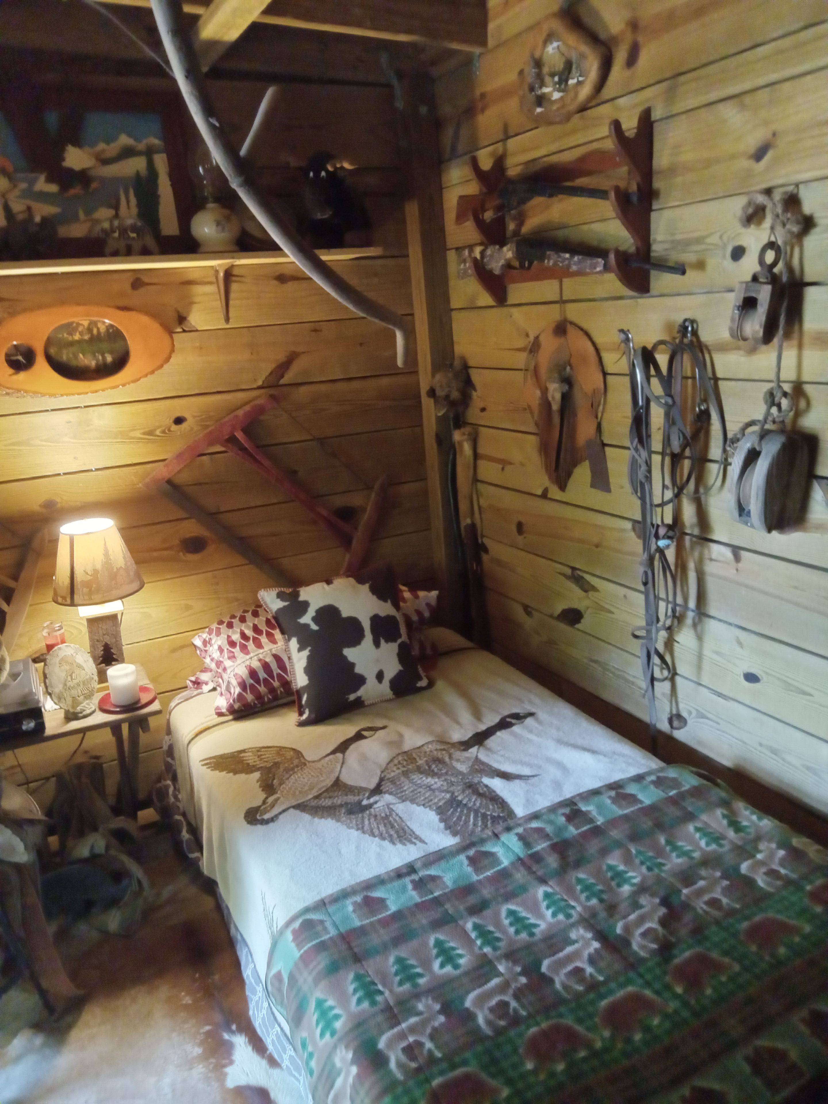 Une pièce rustique en bois, avec un lit, une lampe et des accessoires de chasse accrochés au mur.