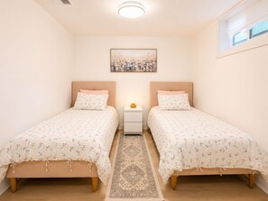 Een slaapkamer met twee bedden, een nachtkastje, een vloerkleed en een schilderij aan de muur.
