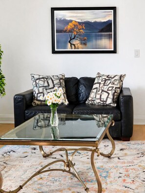 A black leather sofa with patterned cushions, a glass coffee table, and a framed landscape painting on the wall. - Self-Contained, Full Kitchen, Full Bath, Private-B (Richmond Hill)
