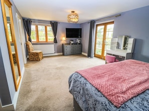 A bedroom with a bed, a chair, a dresser, a television, and a window with curtains. - Hazeldene (Evesham)
