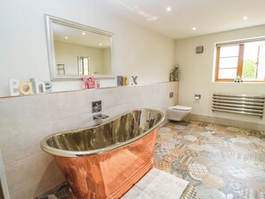 A bathroom with a freestanding bathtub, a toilet, a radiator, and a window. - Hazeldene (Evesham)