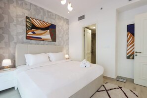 A hotel room with a large bed, a nightstand, a wall-mounted abstract painting, and a door to the bathroom. - Upgraded 1BR with Pool & Free Parking | JVC (Dubai)