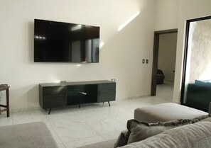 A modern living room with a flat-screen TV mounted on the wall, a dark-colored entertainment unit, and a large window providing natural light. - San Carlos Villa de Lobos - Pool•BBQ•Sleeps 14 (Villa Bemela)
