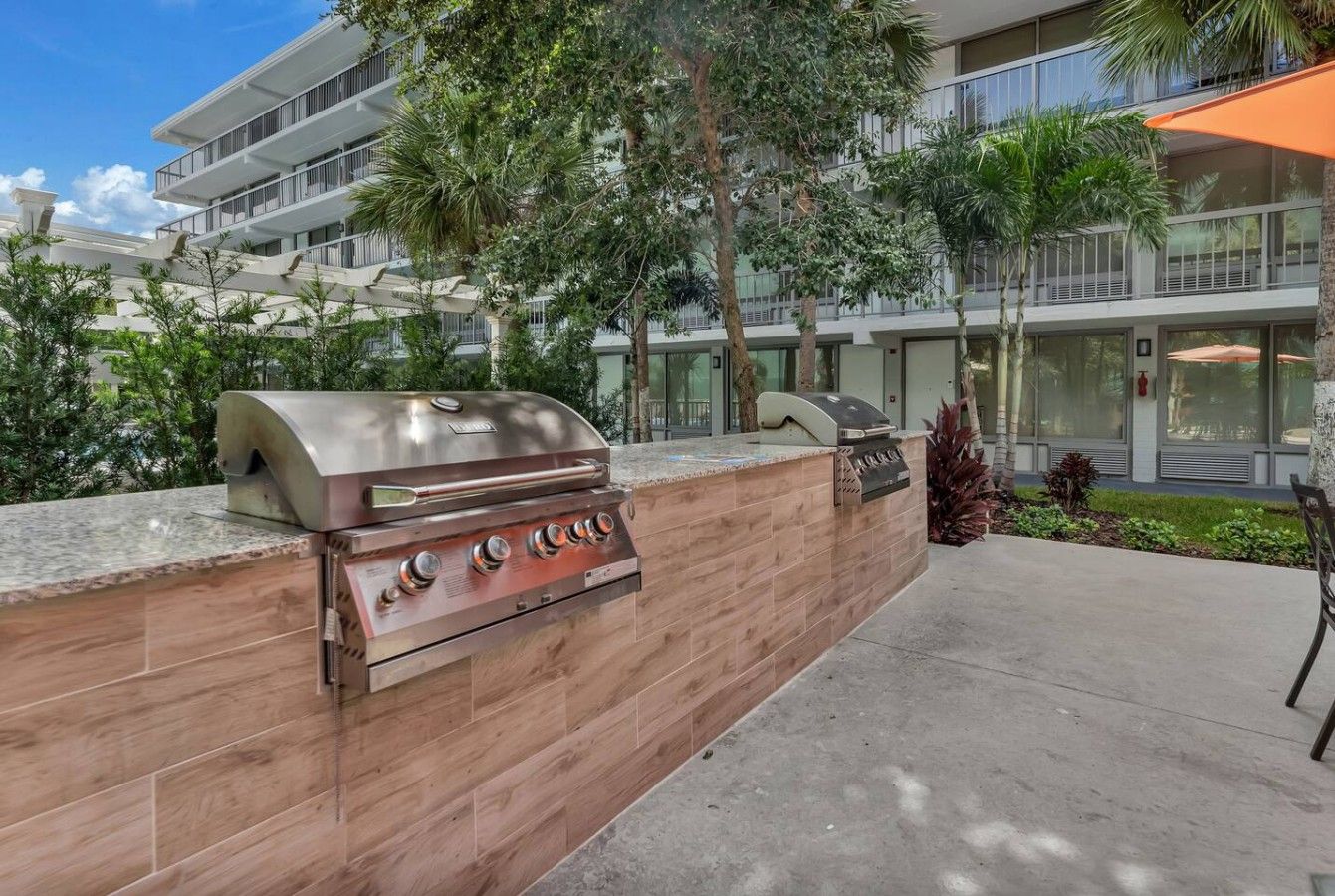 Un espacio de parrilla al aire libre con muro de piedra, una parrilla y zona de estar con mesa y sillas.