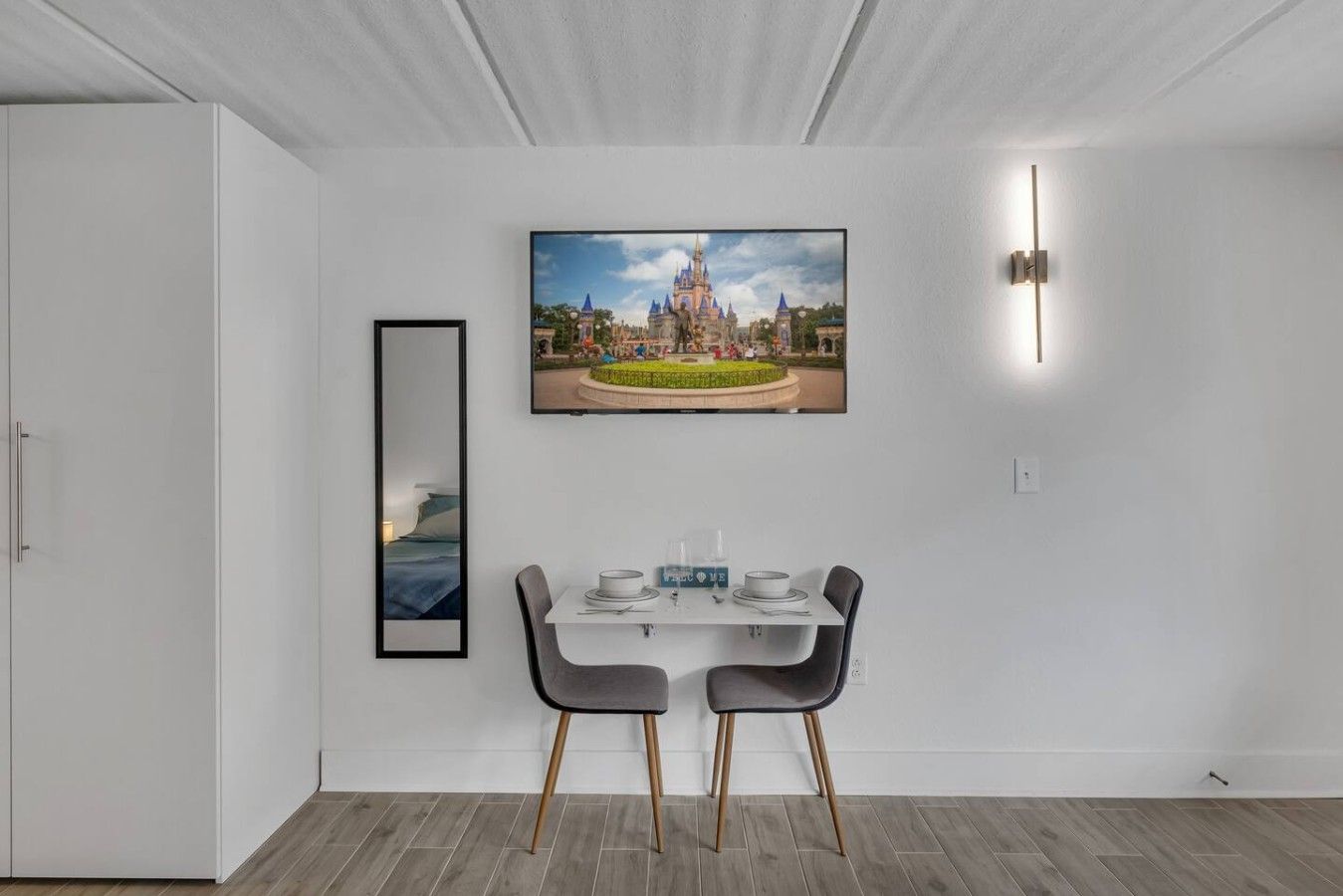 Un coin repas avec une table dressée pour deux personnes, un tableau encadré au-dessus de la table et un luminaire moderne fixé au mur.