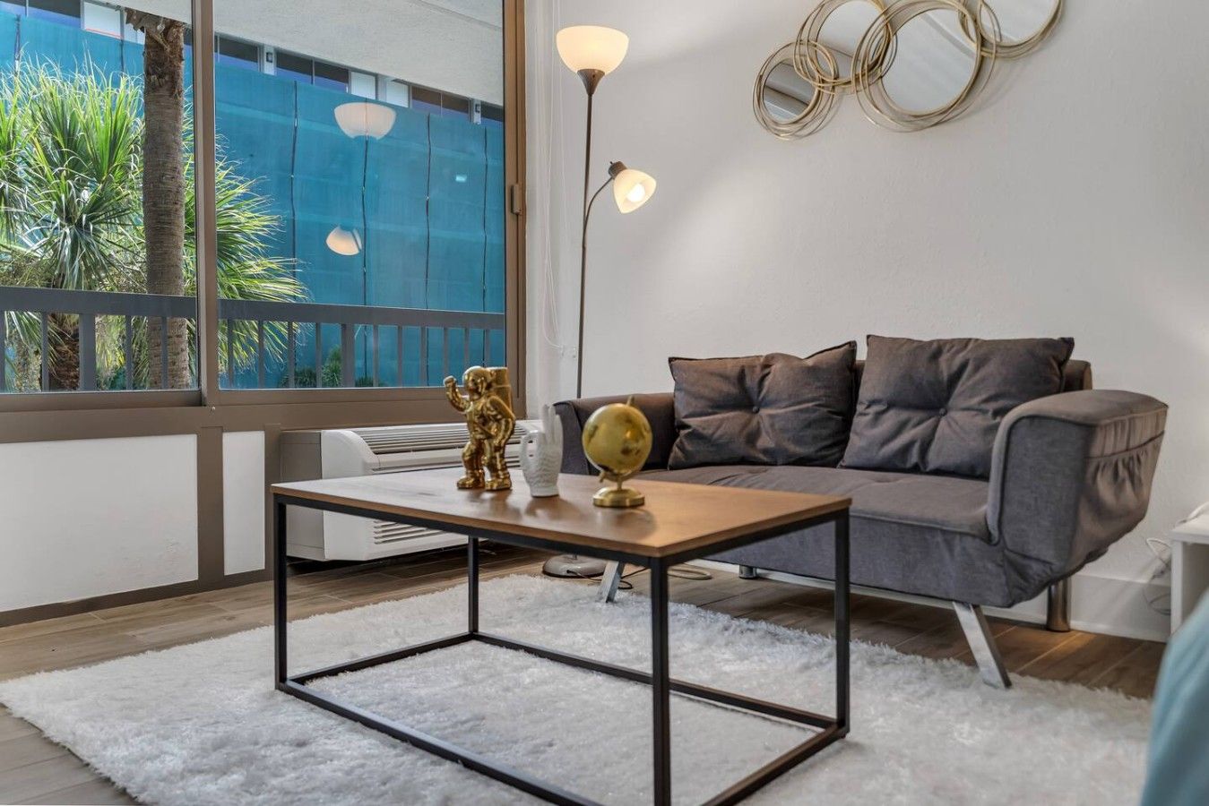 A modern living room with a sofa, a coffee table, decorative items, and a large window with a view of greenery.