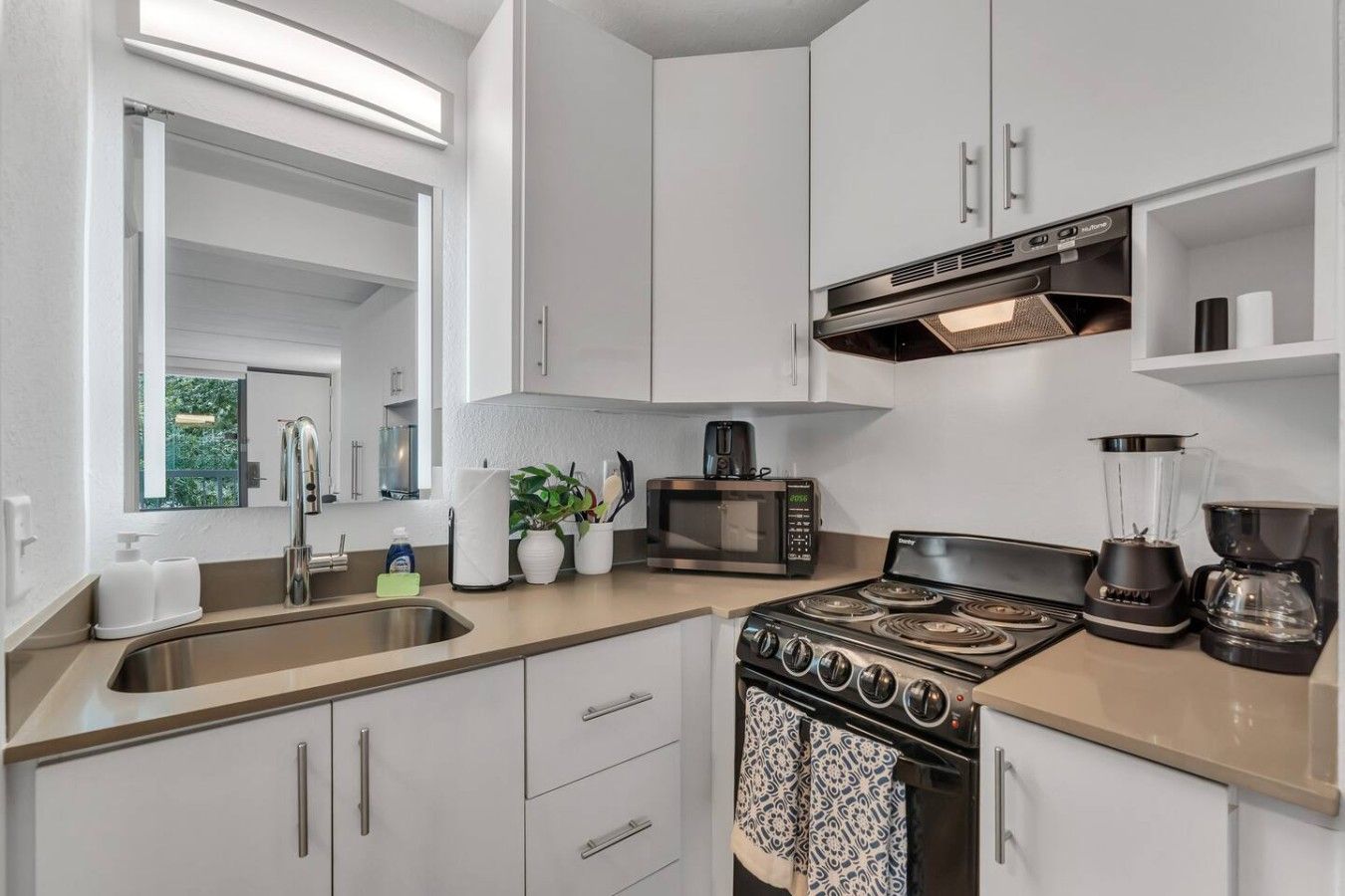 A modern kitchen with a stainless steel sink, a microwave, a stove, and a coffee maker.