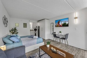 A modern hotel room with a bed, a desk, a chair, a coffee table, and a TV. - Orlando Studio | Disney Nearby + Resort Pool | Orl (Kissimmee)