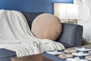Ein Zimmer mit einem grauen Sofa, einem beigen Kissen und einer weißen Decke.